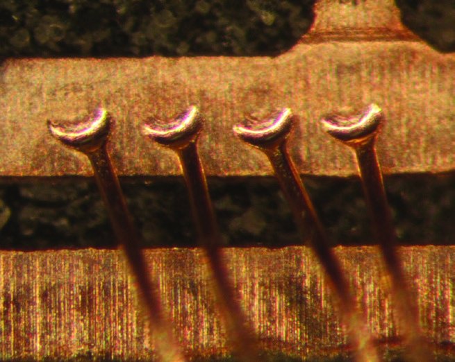 Copper wire bonds fully exposed at the bond pads, with wire stems and ball bonds intact after processing.